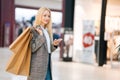 Smiling attractive blonde young woman in stylish coat holding mobile phone and shopping paper bags with purchases Royalty Free Stock Photo