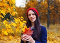 Smiling attractive brunette woman in red hat holding maple leaves in both hands. Autumn concept Royalty Free Stock Photo