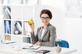 Smiling attractive businesswoman holding apple in office and looking Royalty Free Stock Photo