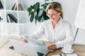 smiling attractive businesswoman reading newspaper at table with laptop Royalty Free Stock Photo