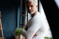 Smiling attractive Casual Grey-haired mature man standing near window looking at the camera.