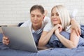 Smiling attractive couple lying on bed using laptop communicating online at home, happy man and woman typing on computer Royalty Free Stock Photo