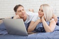 Smiling attractive couple lying on bed using laptop communicating online at home, happy man and woman typing on computer Royalty Free Stock Photo