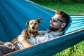 Smiling attractive European man in sunglasses is resting in hammock with his cute little dog Royalty Free Stock Photo