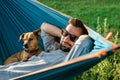 Smiling attractive European man in sunglasses is resting in hammock with his cute little dog Royalty Free Stock Photo