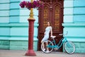 Smiling attractive girl posing next to blue vintage bike near old historical blue building with red antique doors. Royalty Free Stock Photo