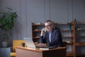 Smiling attractive grey hair elderly man in glasses working on laptop while talking on mobile phone. Multi-tasking concept Royalty Free Stock Photo