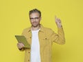 Smiling attractive matured man in yellow jacket pointing above and holding tablet over yellow background Royalty Free Stock Photo