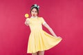 Smiling attractive pinup girl in yellow dress showing sweet lollipop Royalty Free Stock Photo