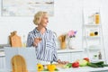 smiling attractive senior woman holding glass of white wine in kitchen Royalty Free Stock Photo