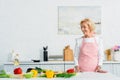 smiling attractive senior woman standing at kitchen counter and looking