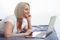 Smiling attractive woman lying on bed using laptop communicating online at home, happy girl typing on computer, enjoying Royalty Free Stock Photo