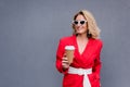 smiling attractive woman in red jacket holding disposable coffee cup
