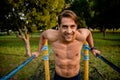 Smiling attractive young male athlete building arm muscle strength using horizontal bars in outdoor park