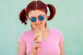 Smiling audacious young woman with pigtails hairstyle holds ice-cream in waffle cone, it reflects in her sunglasses. Urban style Royalty Free Stock Photo