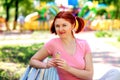 Smiling young woman with pigtails hairstyle and pink shirt sitting on bench in park and holding ice-cream in waffle cone