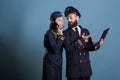 Smiling aviator using laptop while stewardess talking on smartphone