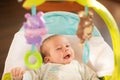 A smiling baby boy lieing in the swinger and looking at the toys