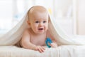 Smiling baby boy after shower or bath with teether toy covered towel in nursery. Health care concepts.