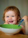 Smiling baby eating food. Funny baby eating food himself with a spoon on kitchen. Healthy nutrition for kids. Launching Royalty Free Stock Photo