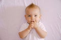 Smiling baby with fingers in mouth lies on the bed. Close-up Royalty Free Stock Photo