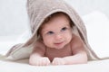 Smiling baby girl after shower with towel on head. Happy laughing baby wearing hooded towel lying on bed after bath