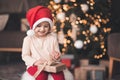 Smiling baby girl wearing santa claus hat and pajamas open xmas present box over Chrismas tree with glowing lights close up. Royalty Free Stock Photo