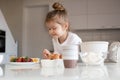 Smiling baby girl 3-4 year old making dough in white bowl for cake on kitchen table at home close up. Royalty Free Stock Photo