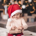 Smiling baby girl 3-4 year old open Christmas present box  wearing red santa claus hat and pajamas over glowing lights close up. Royalty Free Stock Photo