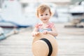 Smiling baby girl 1-2 year old wear striped dress and holding straw hat over wooden pier at sea shore outdoors. Royalty Free Stock Photo