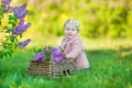 Smiling baby girl 1-2 year old wearing flower wreath, holding bouquet of lilac outdoors. Looking at camera. Summer spring time. Royalty Free Stock Photo