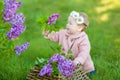 Smiling baby girl 1-2 year old wearing flower wreath, holding bouquet of lilac outdoors. Looking at camera. Summer spring time. Royalty Free Stock Photo