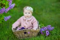 Smiling baby girl 1-2 year old wearing flower wreath, holding bouquet of lilac outdoors. Looking at camera. Summer spring time. Royalty Free Stock Photo