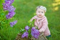 Smiling baby girl 1-2 year old wearing flower wreath, holding bouquet of lilac outdoors. Looking at camera. Summer spring time. Royalty Free Stock Photo