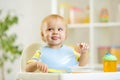 Smiling baby kid boy eating itself with spoon