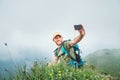 Smiling backpacker man taking selfie picture using smartphone and showing Thumbs Up during walking by the foggy cloudy weather Royalty Free Stock Photo