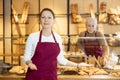 Smiling bakeshop saleswoman in maroon apron offering baked goods