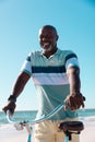 Smiling bald african american senior man riding bicycle at beach under clear blue sky on sunny day