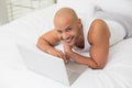 Smiling bald man using laptop in bed Royalty Free Stock Photo