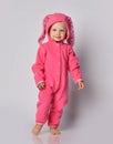 Smiling barefooted blonde baby girl in pink warm comfortable jumpsuit with hood with bunny ears on walks towards camera