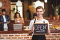 Smiling barista holding chalkboard with open sign