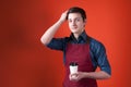 Smiling barista in shirt with rolled sleeves and burgundy apron holding paper cup, looking at camera and straighten hair Royalty Free Stock Photo