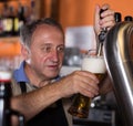 Smiling barman is pouring unbottled beer for next client