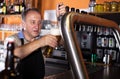 Smiling barman is pouring unbottled beer for next client