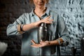 Smiling bartender girl holds metal shaker at bar