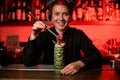 Smiling bartender girl serving alcoholic cocktail in the Tiki mug adding arose bud with tweezers