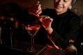 Smiling bartender girl sprinkling on a alcoholic drink in the cocktail glass with a orange zest juice