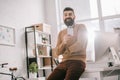 Smiling bearded adult businessman sitting on office desk and holding blank security tag