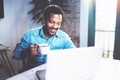 Smiling bearded African man using laptop home while drinking cup black coffee at the wooden table.Concept of young Royalty Free Stock Photo