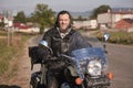 Smiling bearded biker in black leather jacket sitting on modern motorcycle on country roadside. Royalty Free Stock Photo